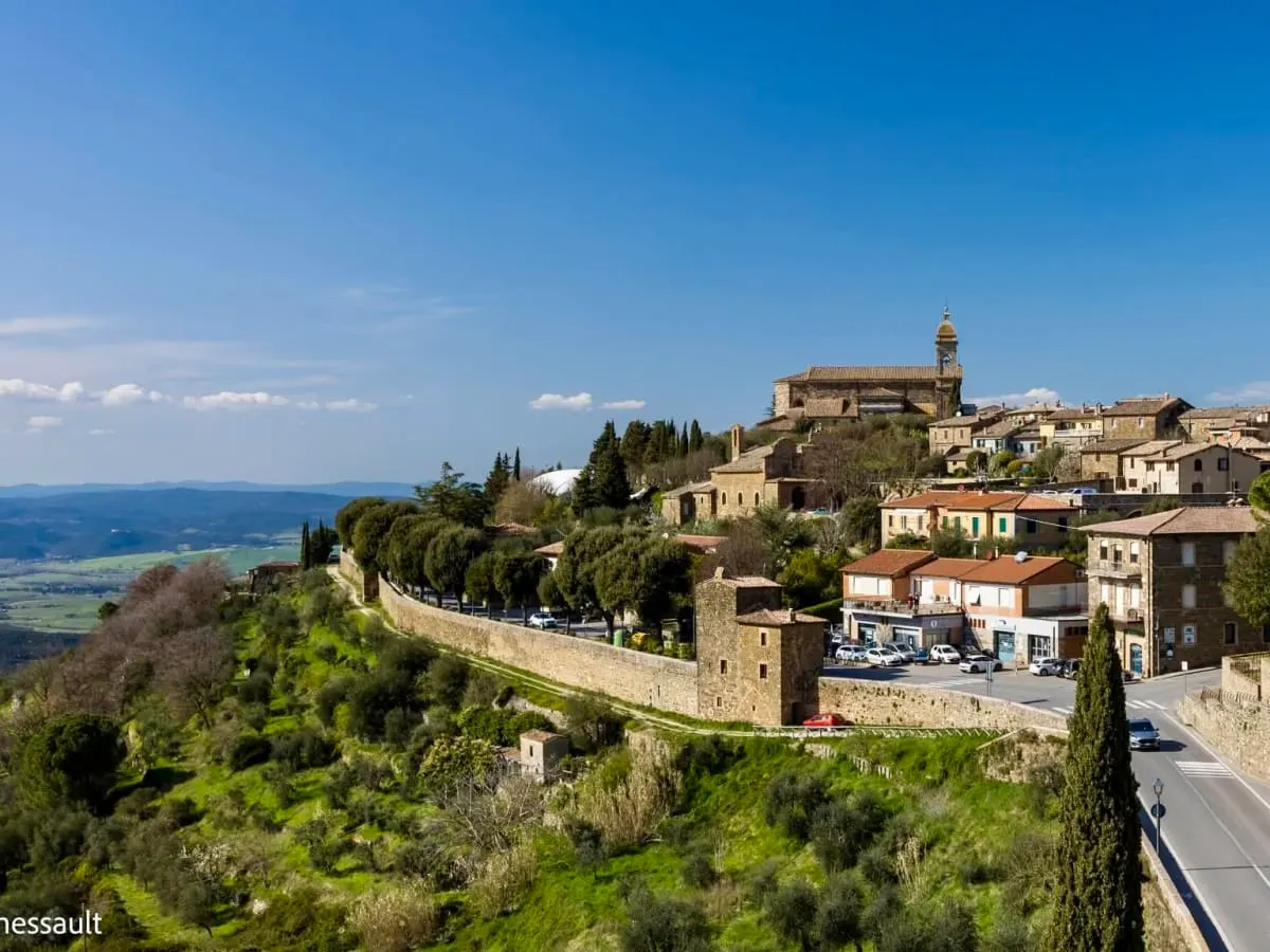 Cette photographie présente un magnifique village perché de Toscane, installé au sommet d'une colline et dominant un vaste paysage de vallées verdoyantes.
