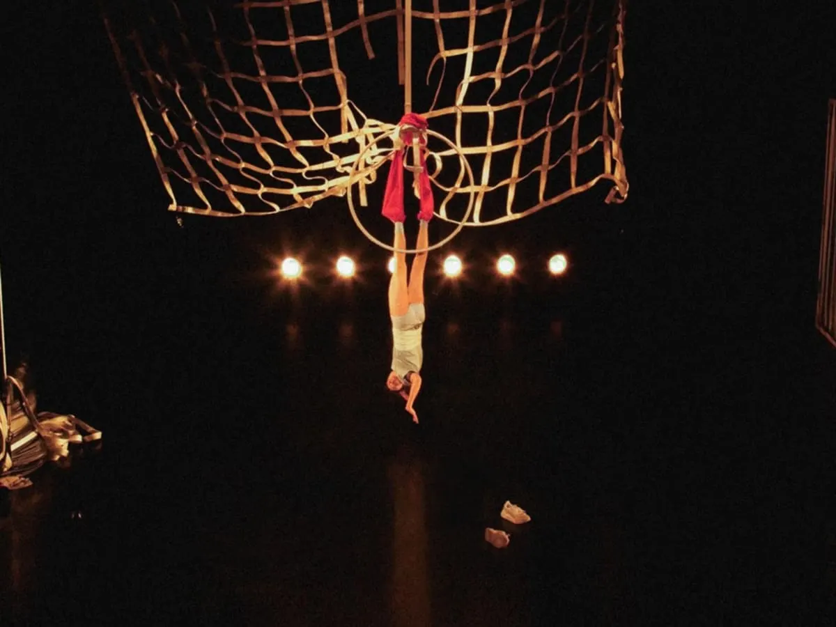 Acrobate suspendu par les pieds avec un ruban rouge, sous un immense filet.
