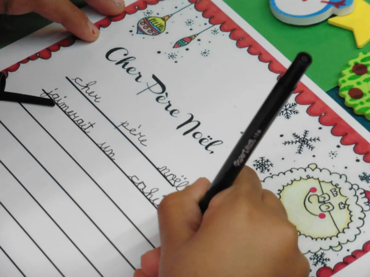 Une petite main qui tient un stylo, qui écrit au Père Noël