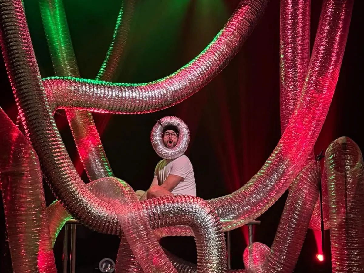 Un artiste se tient parmi des tuyaux métalliques sur scène.