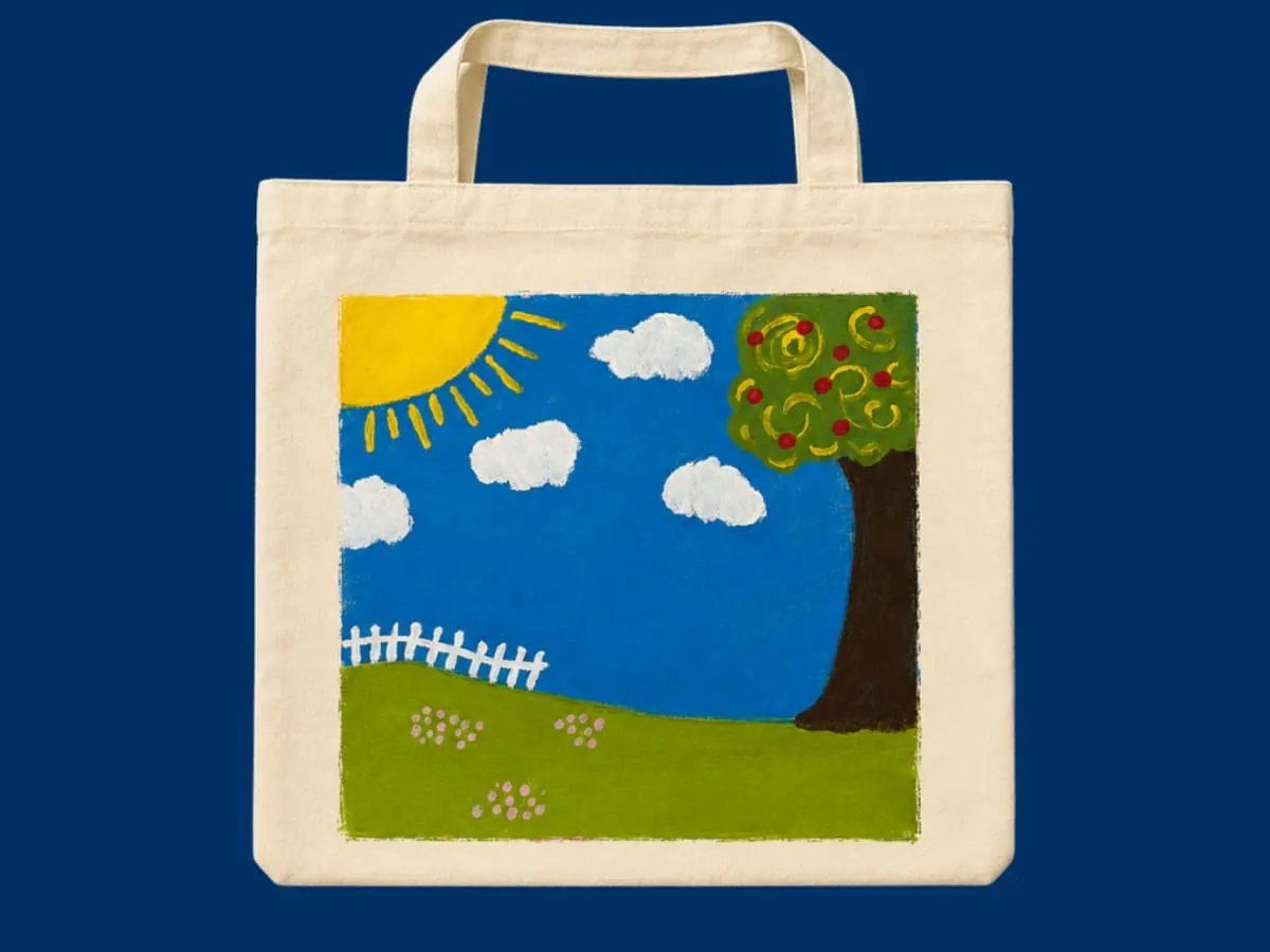 Photographie d'un sac en tissu avec une peinture faite à la main représentant un paysage ensoleillé, le sac est posé sur un fond bleu foncé.