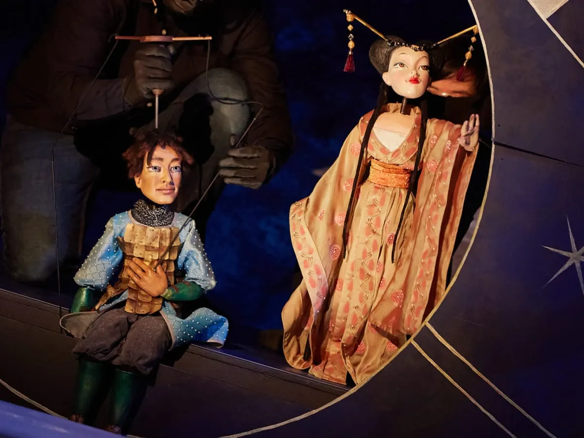 Marionnettes manipulées sur scène incarnant des personnages dans une scénographie théâtrale riche en détails et costumes.
