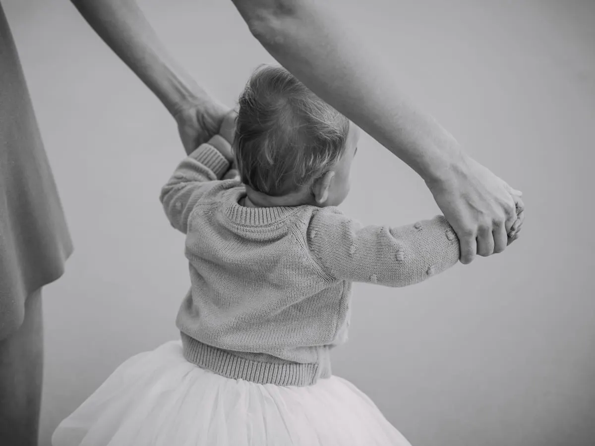 Photo en noir et blanc d'un poupon qui porte une veste et un tutu qui tient les mains d'un adulte